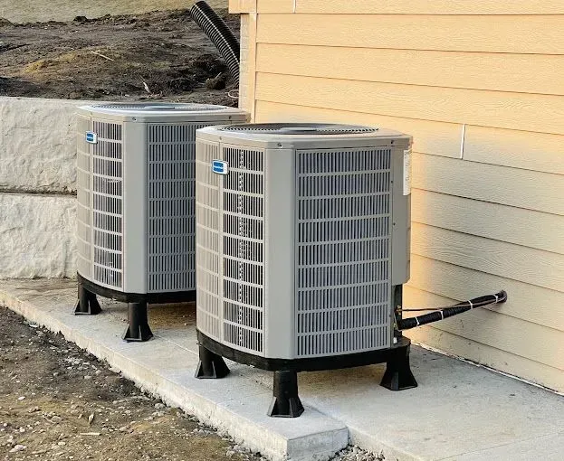 Two gray air conditioning units sitting on concrete near a building.