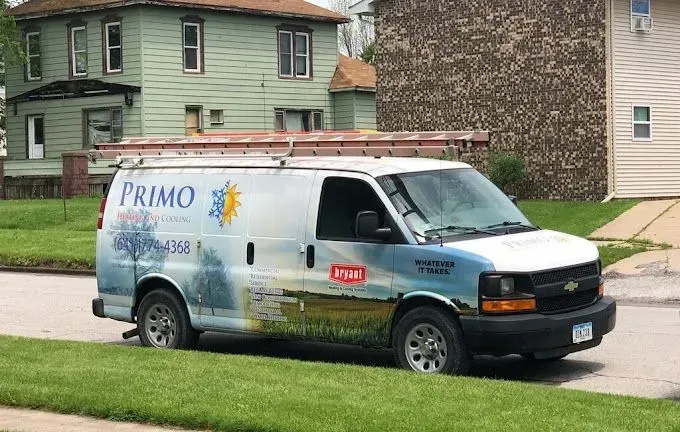 White van with ladder, Primo logo, parked on a street in front of a green house.