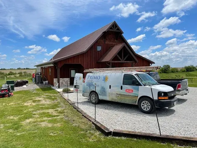 Barn-style building with a brown roof and a white van parked in front, under a blue sky.