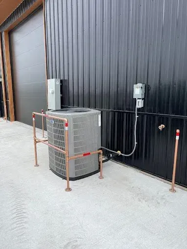 Exterior air conditioning unit with copper protective cage, attached to black building.