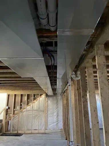 Framed basement ceiling with HVAC ductwork, pipes, and electrical wiring installed. Stud walls visible.