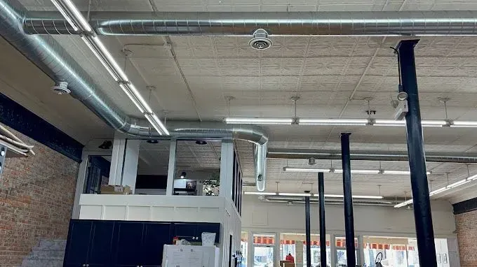 Interior view of a commercial space under construction with exposed ductwork, support columns, and overhead lighting.