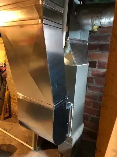 Two rectangular metal HVAC ducts, one angled, installed on a brick wall in a basement.