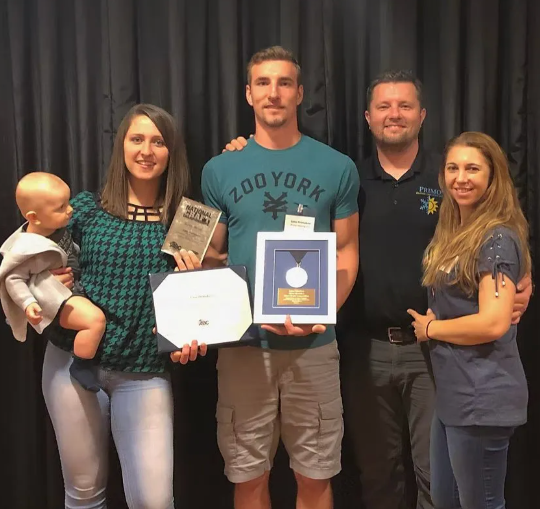 Man wearing glasses and a suit, looking at the camera with a neutral expression. Dark background.