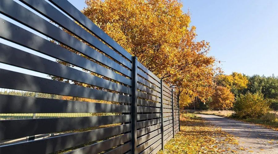 Black residential aluminum fence on a sloping backyard lawn with colorful autumn