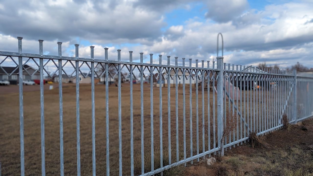 Galvanized metal fence encloses a grassy area. Cloudy sky in the background.
