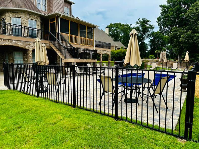A fence surrounds a patio with tables and chairs and umbrellas.
