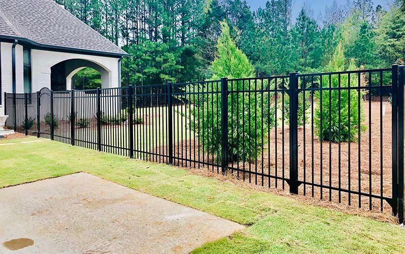 A black metal fence surrounds a lush green yard in front of a house.