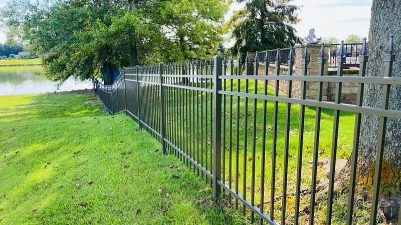 A metal fence surrounds a lush green field next to a lake.