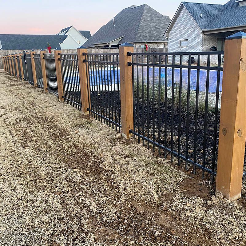 A metal fence with wooden posts is surrounding a pool in a backyard.