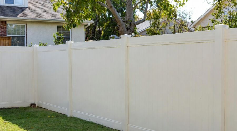 A tall, off-white vinyl privacy fence borders a green lawn in a suburban backyard.