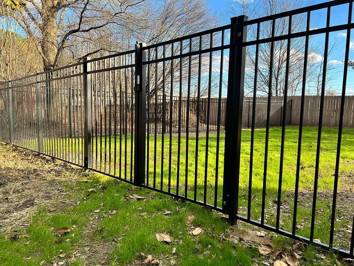A black wrought iron fence surrounds a lush green field.