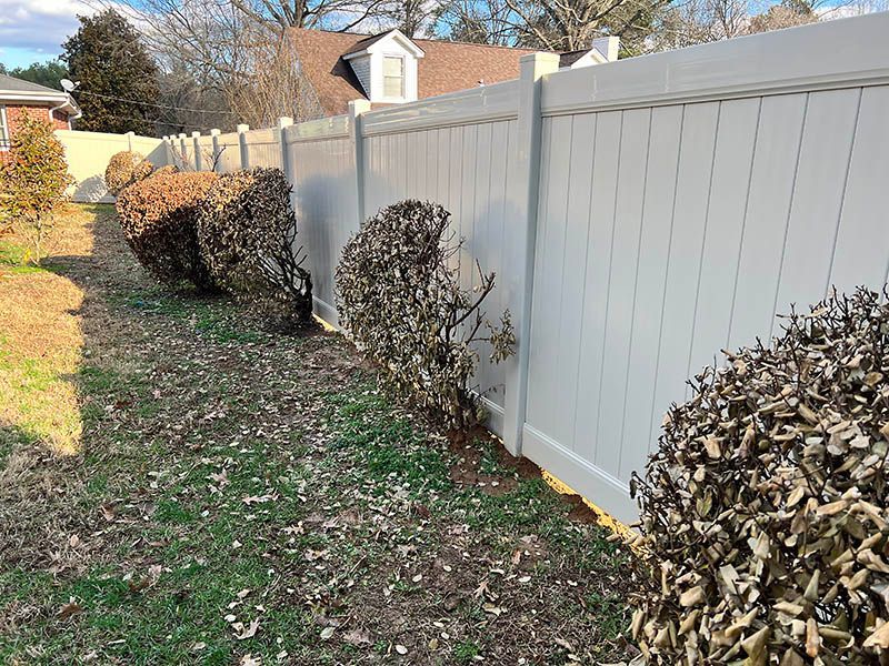 A white vinyl fence is surrounded by bushes in a backyard.