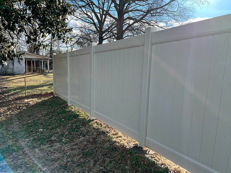 A white vinyl fence surrounds a yard with a house in the background.