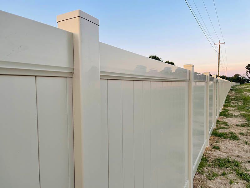 A white vinyl fence is surrounded by grass and power lines.
