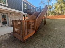 A wooden deck with stairs leading up to it in front of a house.