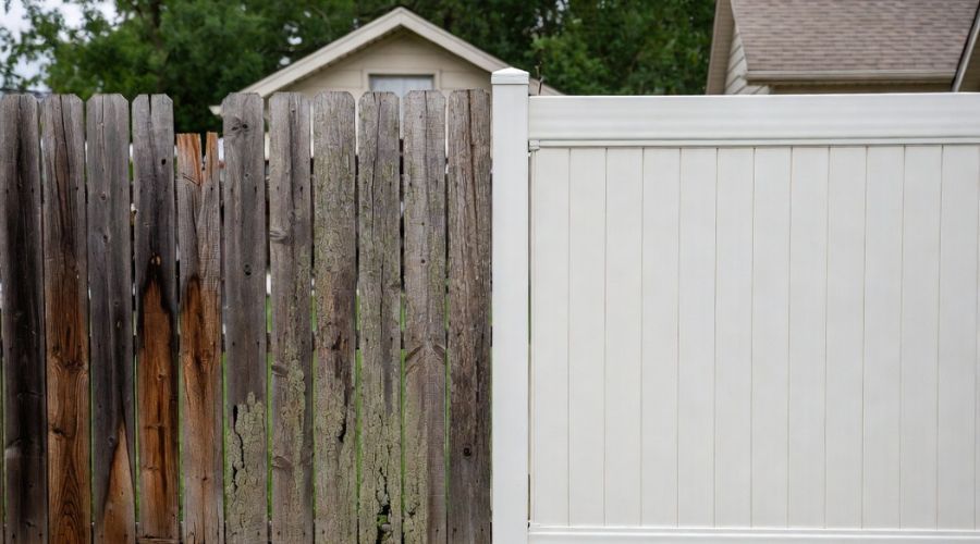 An old, weathered wooden fence standing next to a clean, modern white vinyl privacy fence.