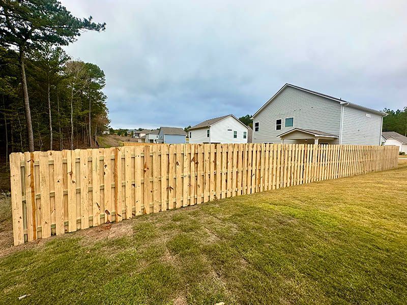 A wooden fence surrounds a grassy field in front of a house.