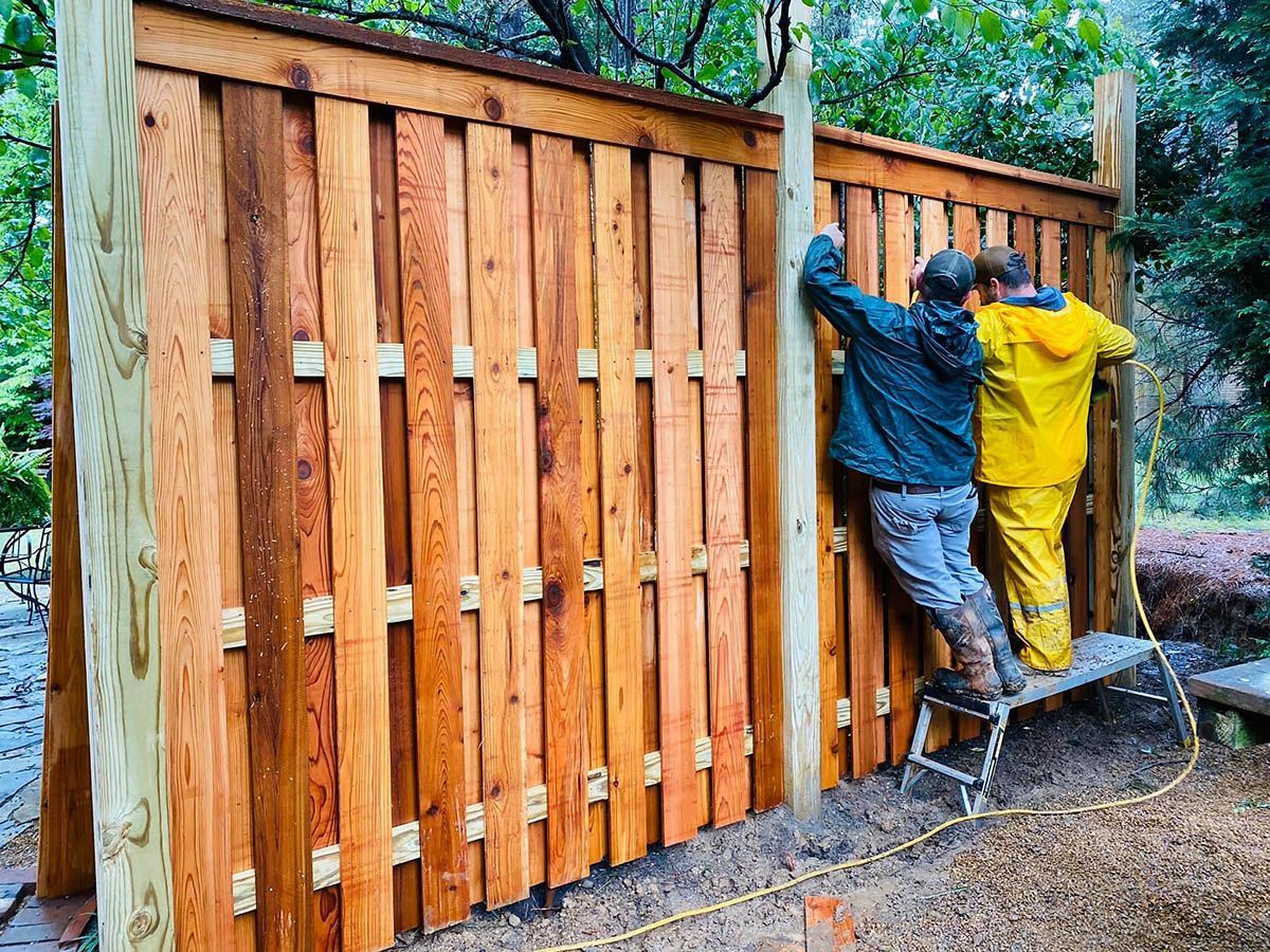 Two men are working on a wooden fence.