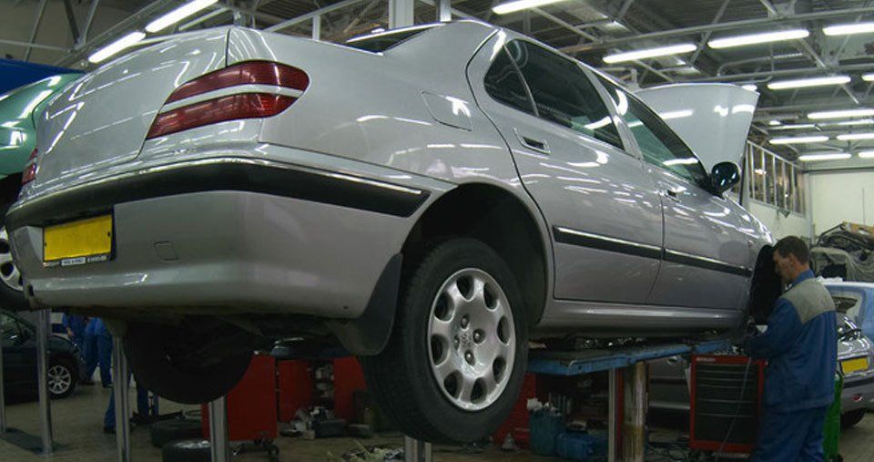 A mechanic working on a silver-grey car on ramps