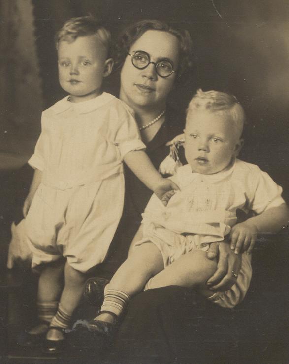Woman in glasses holds two young children; all looking towards the camera.