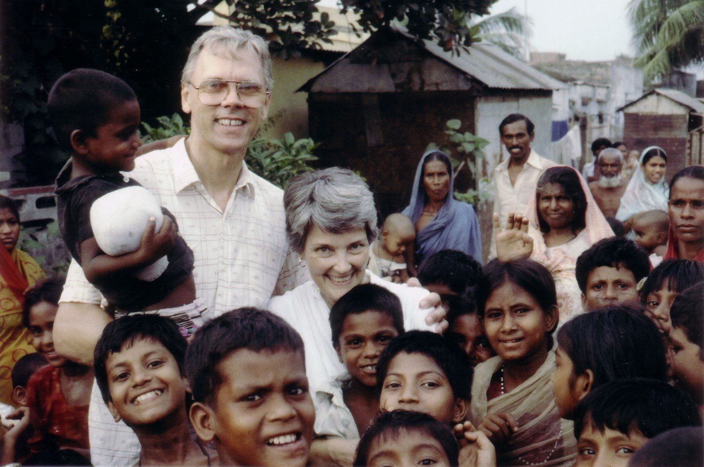 Man and woman surrounded by smiling children; possibly a mission trip in a village setting.