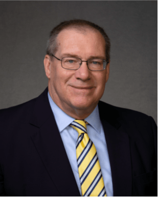 Man in suit and glasses, smiling, blue jacket, yellow striped tie.