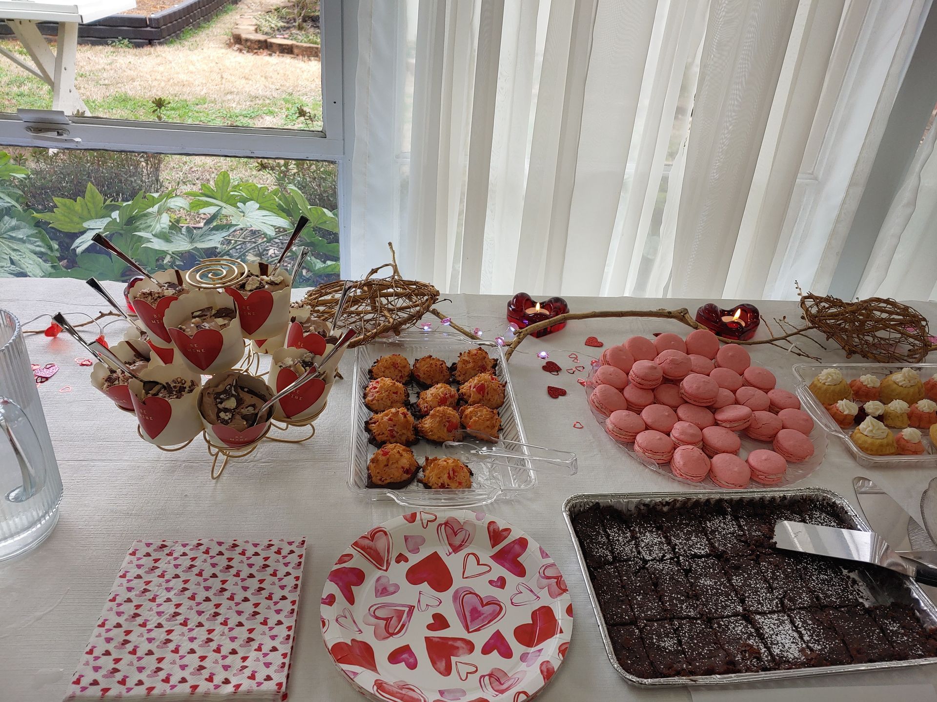 Valentine's Day dessert table with cupcakes, macaroons, brownies, and other treats on a white tablecloth.