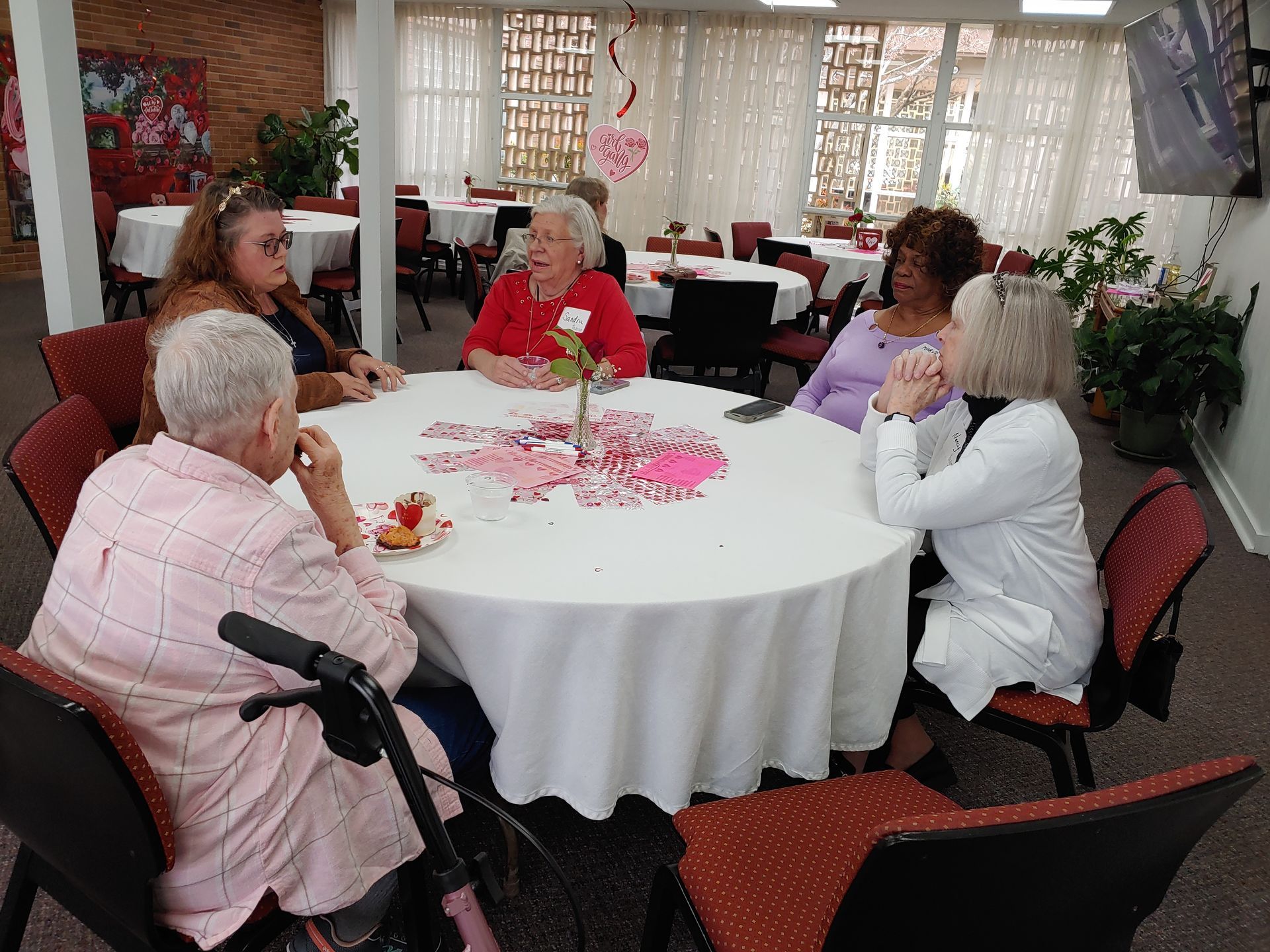 Five people seated around a decorated round table in a room with windows and other tables.