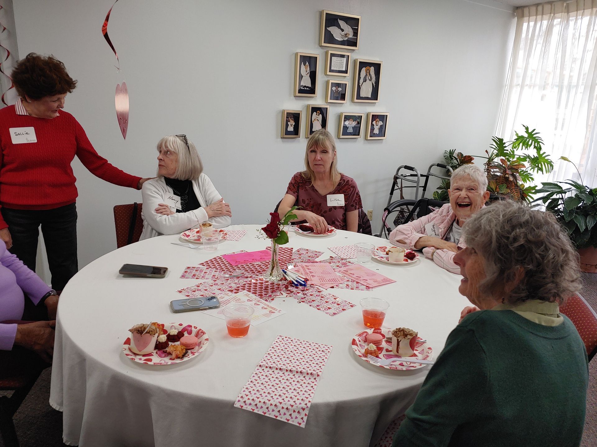 People gathered around a decorated table, celebrating; some are smiling, and one person is touching another's shoulder.