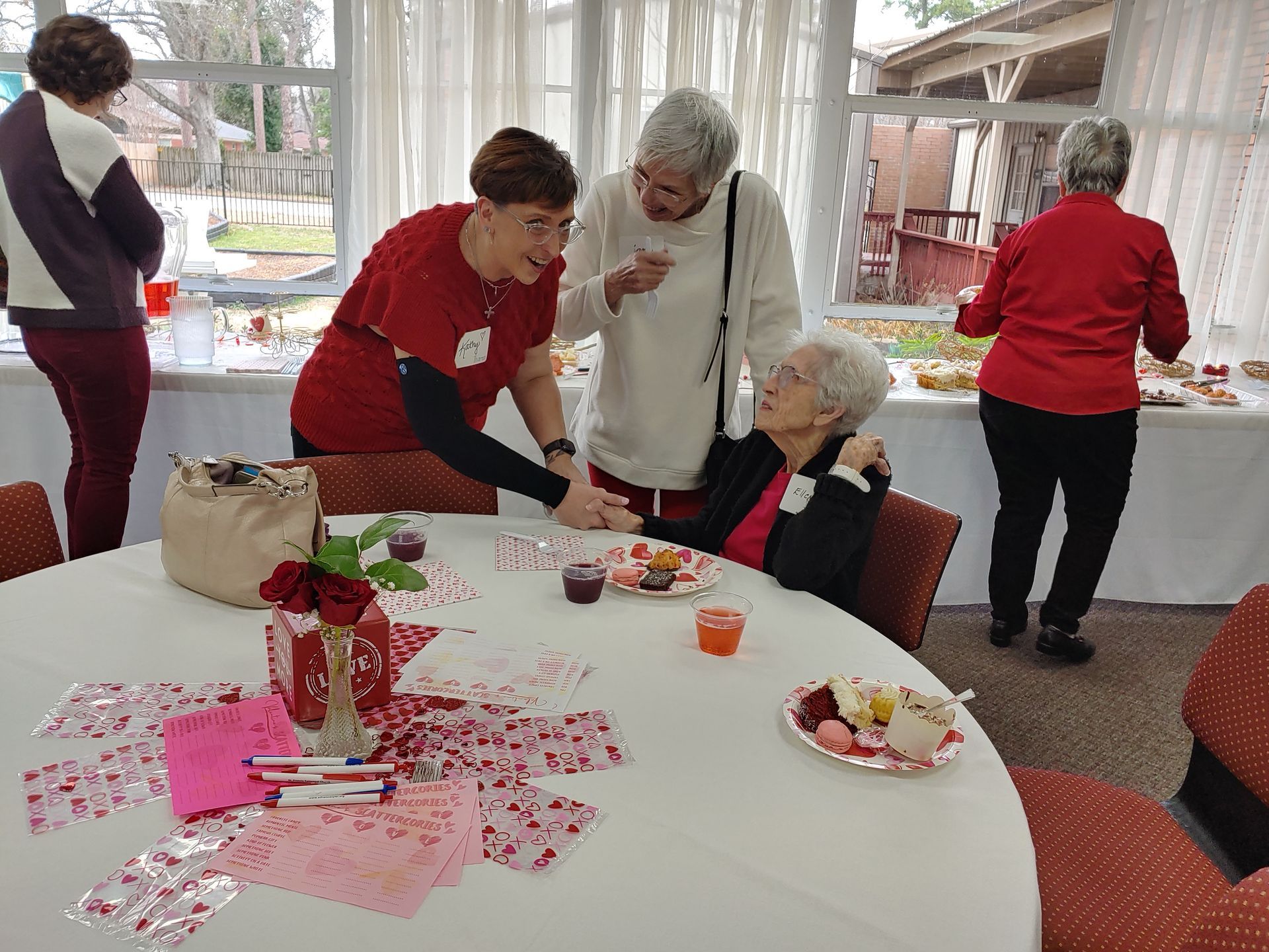 People at a table with Valentine's Day decorations; women looking at food, one person holding another's hand.