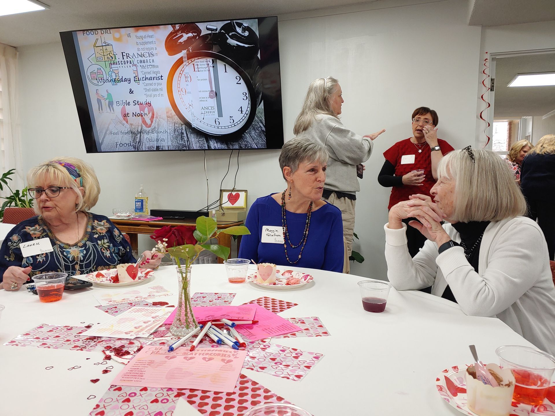 Women seated at a table with Valentine's Day decorations, watching a presentation on a screen.