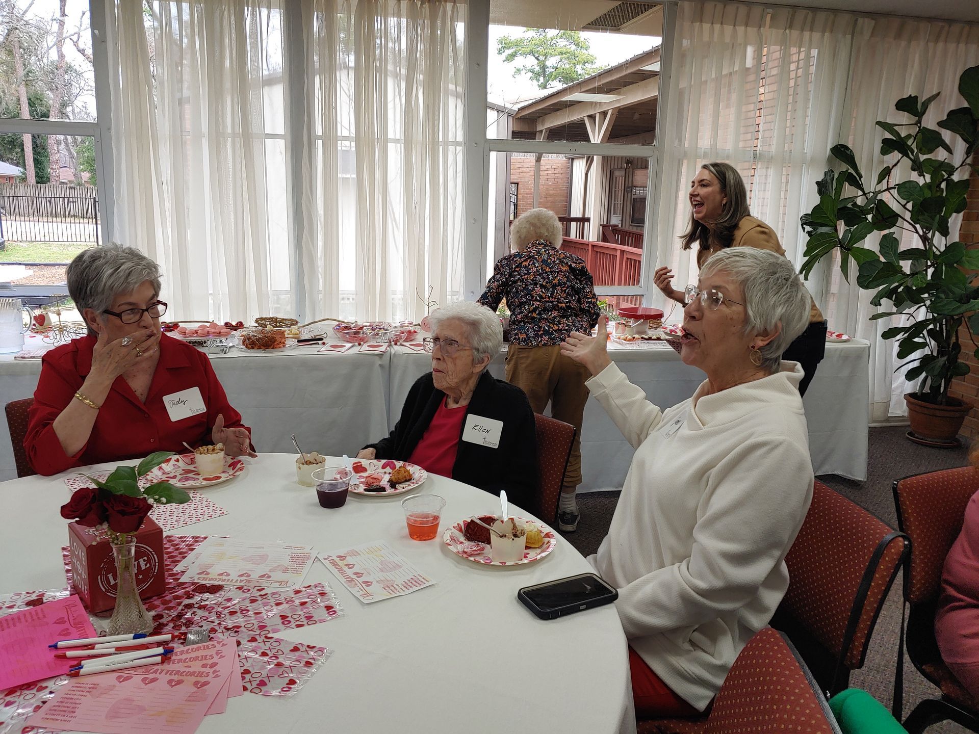 Group of people at a table in a room. Some are eating, others talking. Red and white decor.