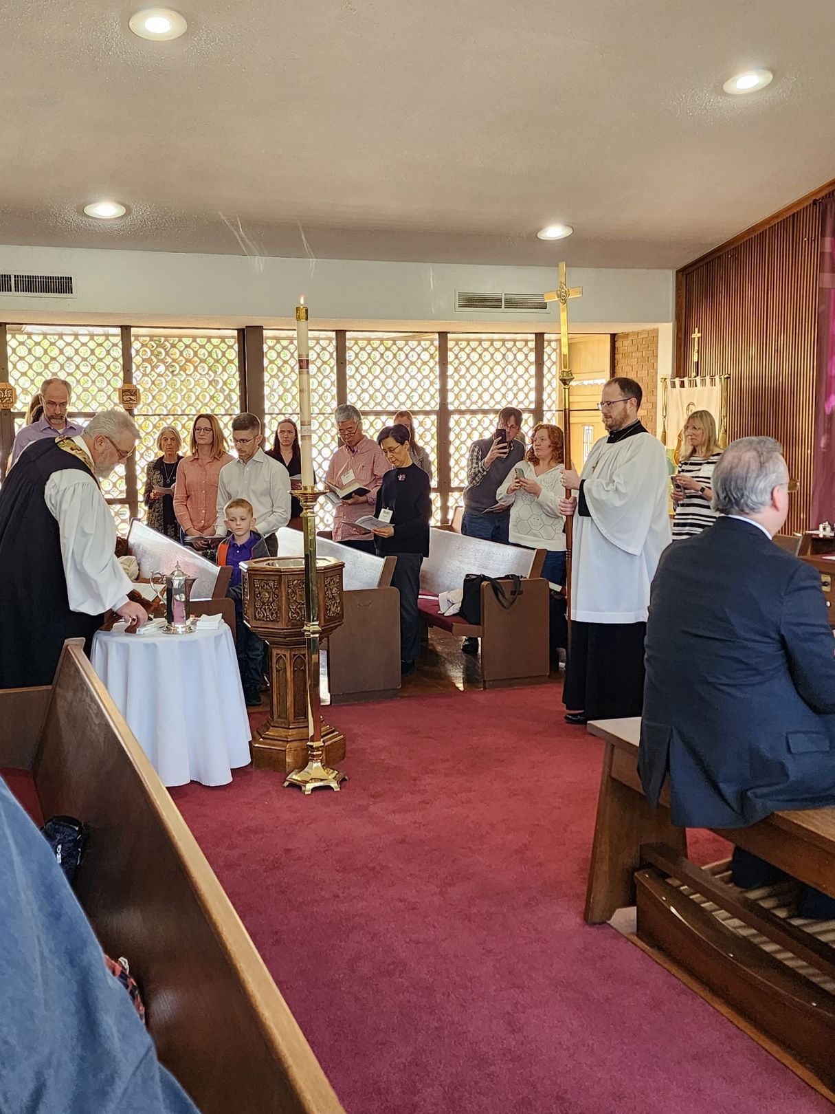 Baptism ceremony in a church. Priest and attendees near a baptismal font. People watching.