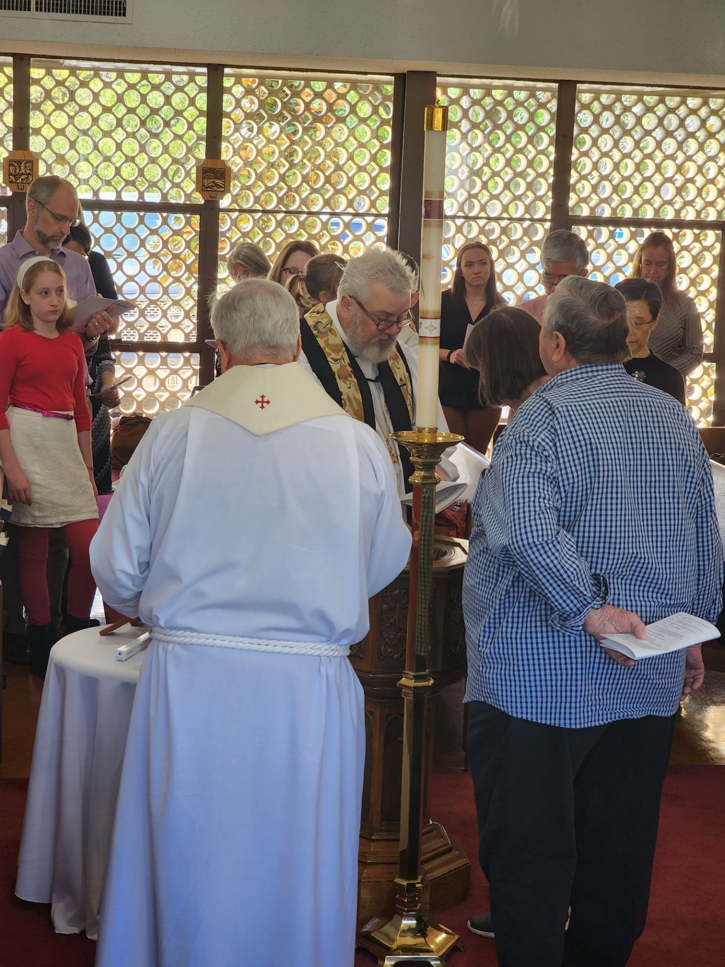 Clergy and parishioners participating in a church ceremony with a tall candle and table.