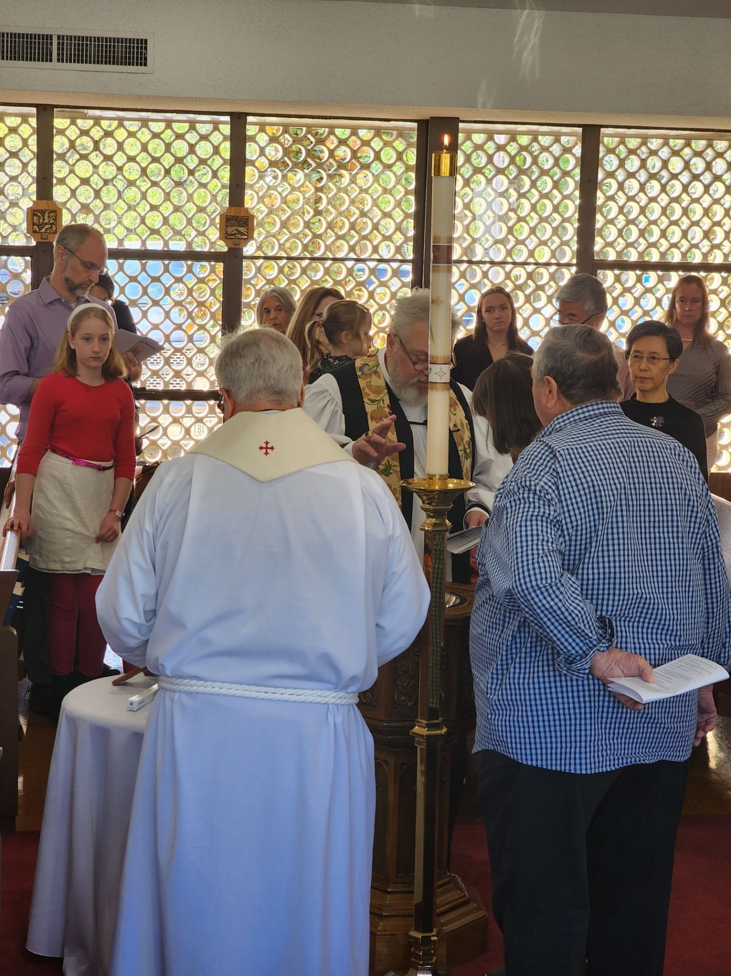 Clergy member leading a baptismal service with other people. Bright sunlight streams through the windows.