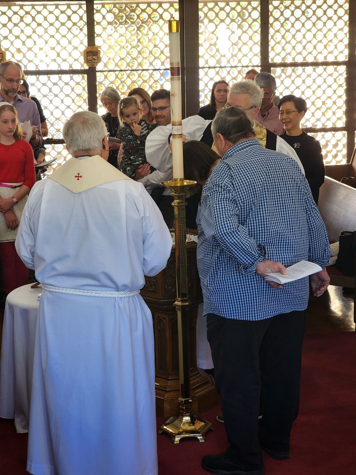 People gathered around a lit candle, possibly at a baptism or religious ceremony.