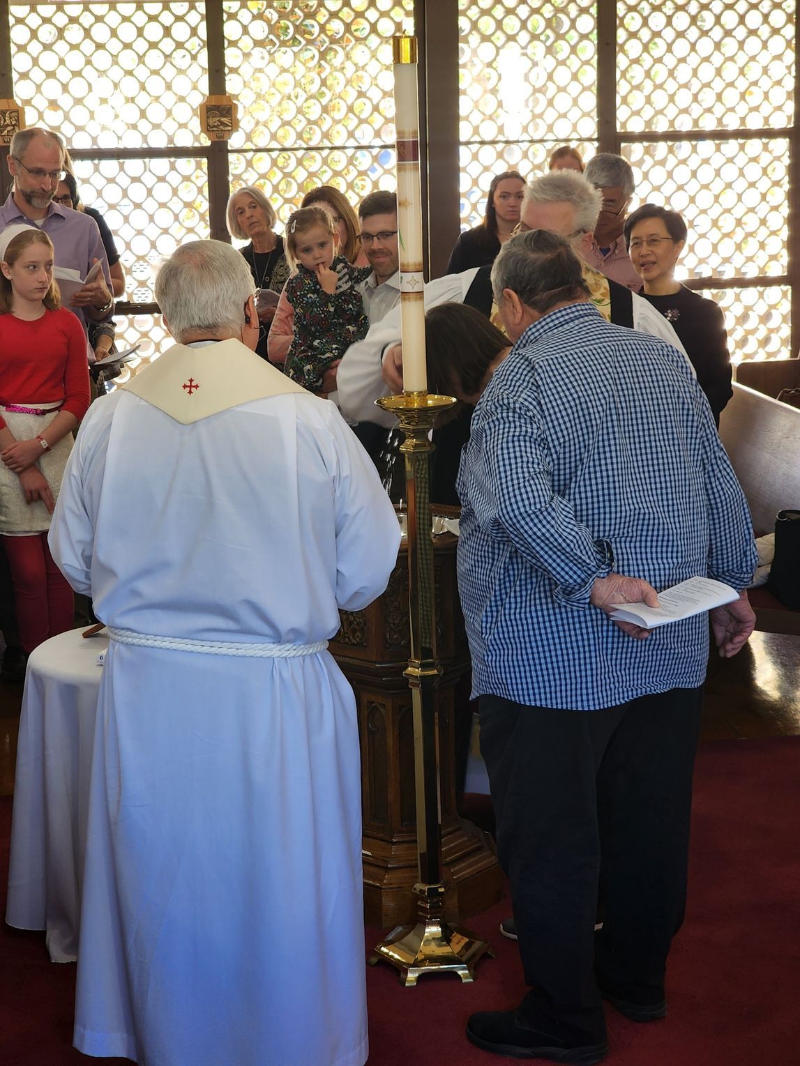 Clergy lighting a candle during a church service; people watch in a sanctuary with stained glass.