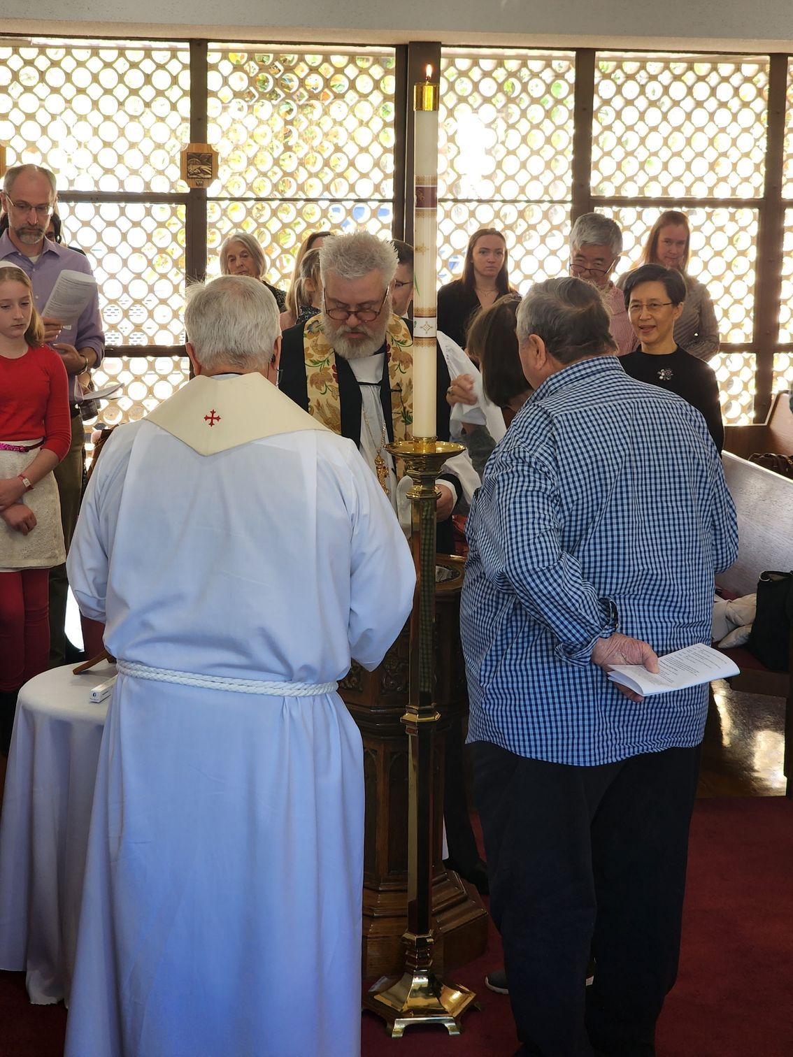 Clergy lighting a candle during a church service; several people witness in front of stained glass windows.