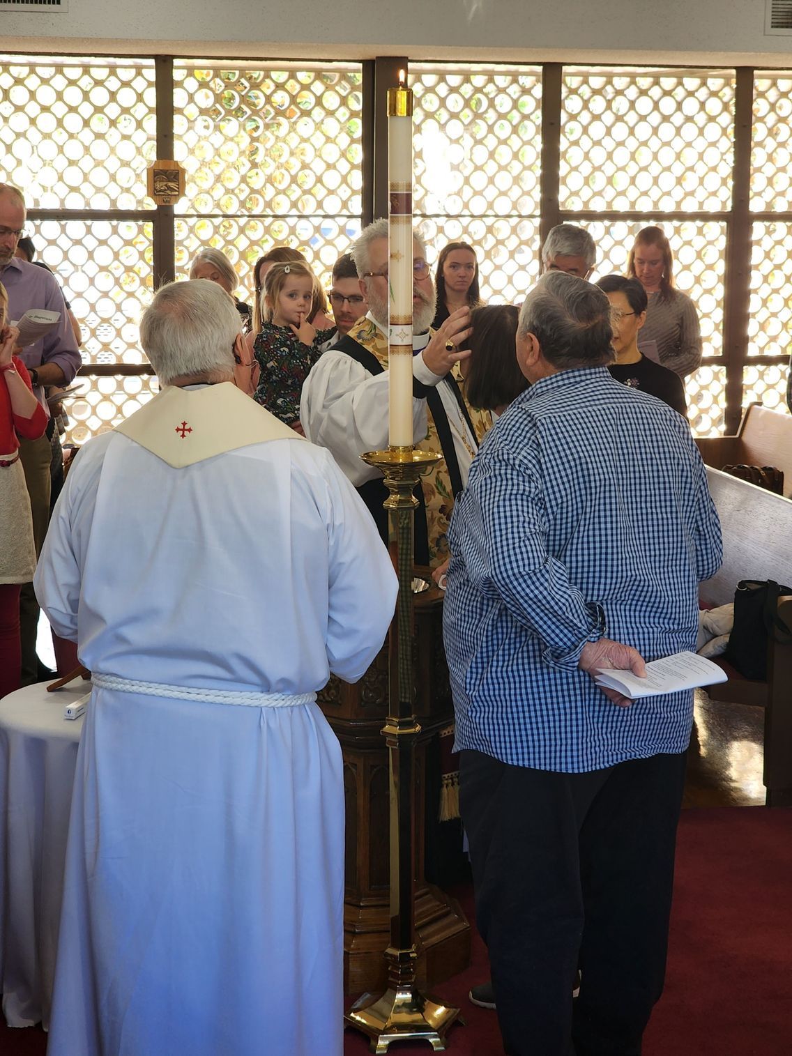 Clergy lighting a candle during a church service with attendees in the background.