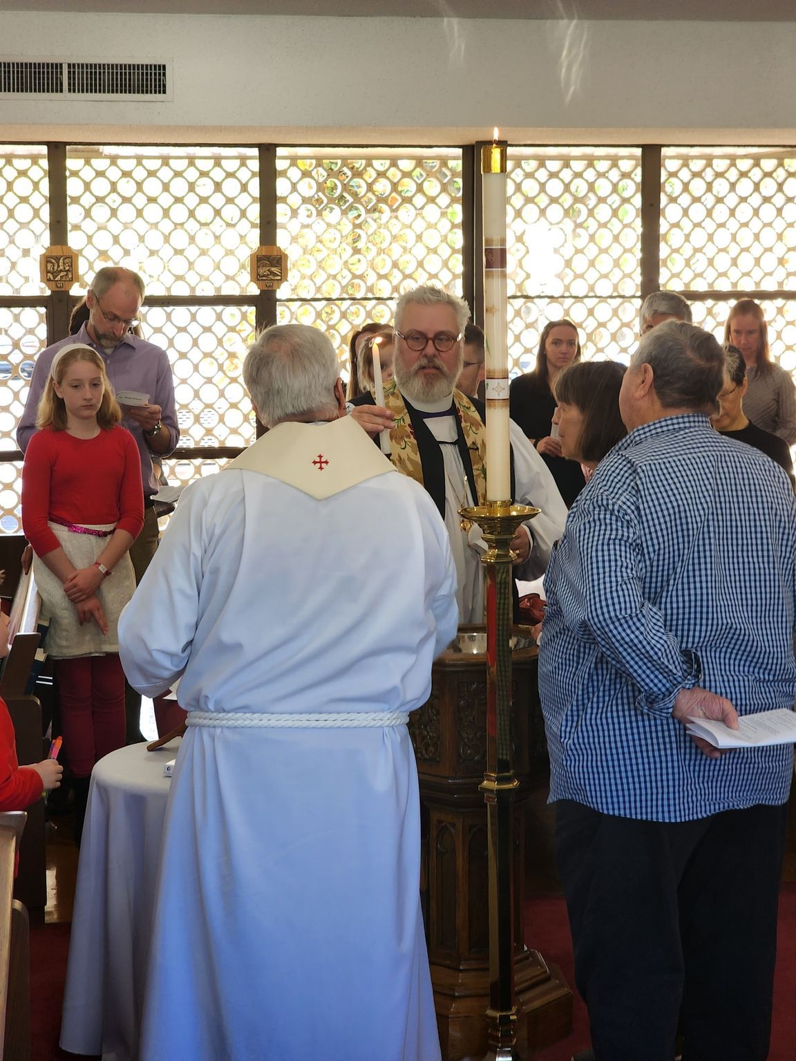 People gathered at a church for a ceremony. A man in robes holds a candle, and others are nearby.