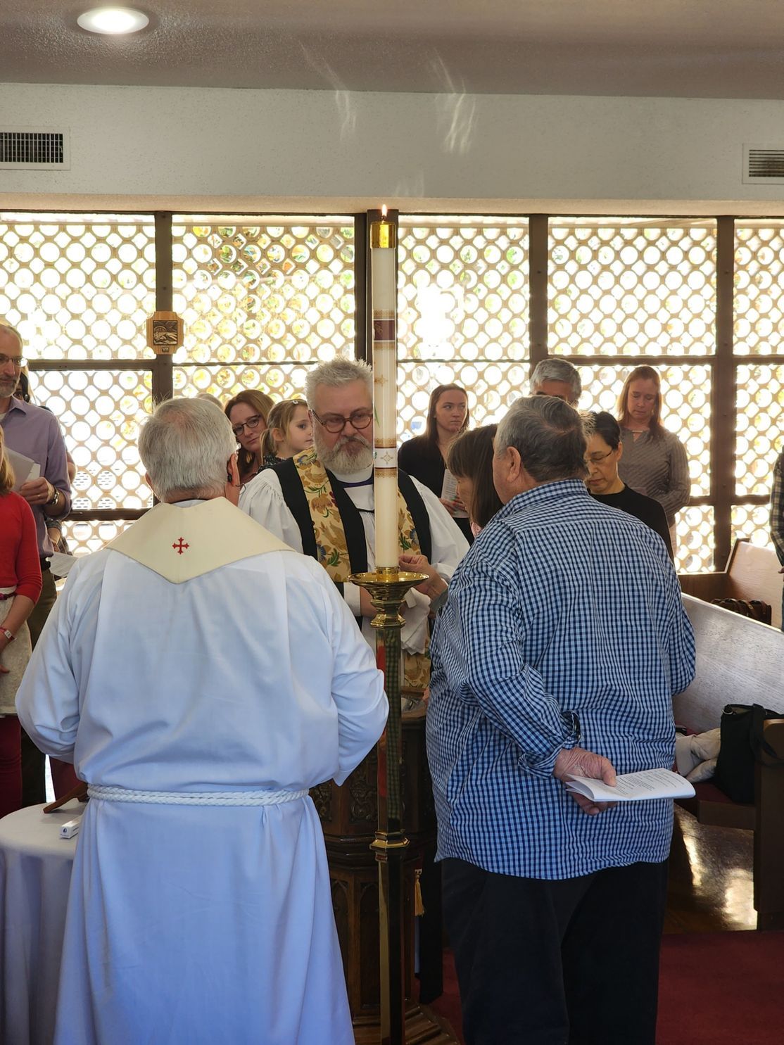 Clergy lighting a candle during a ceremony. Others watch in a well-lit interior space.