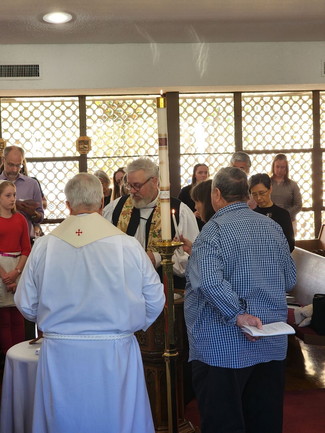 Religious service with clergy near a lit candle, people watching in a church setting.