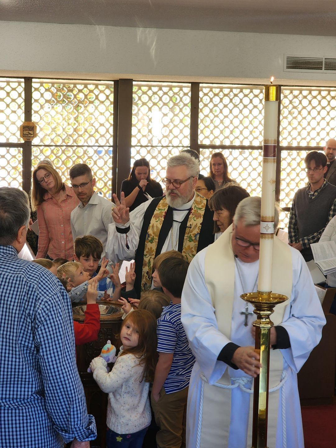 Clergy bless children during a church service. Priest holds a tall candle, others watch.