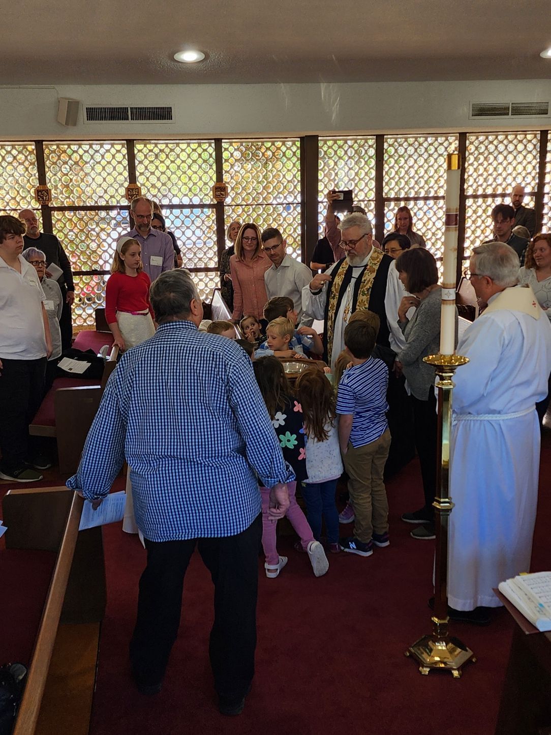 A baptism ceremony in a church. People surround a priest, children are present, warm colors.