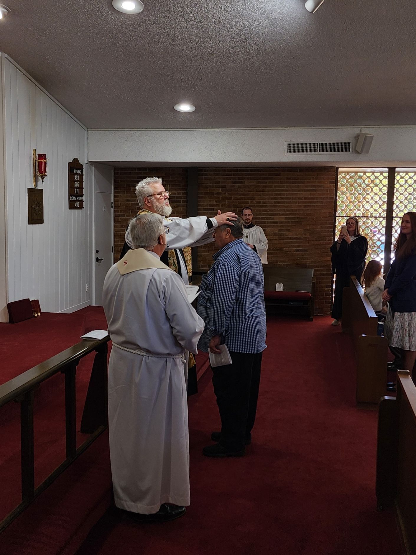 Clergy person laying hands on a man's head during a church service.  Others watch from the pews.