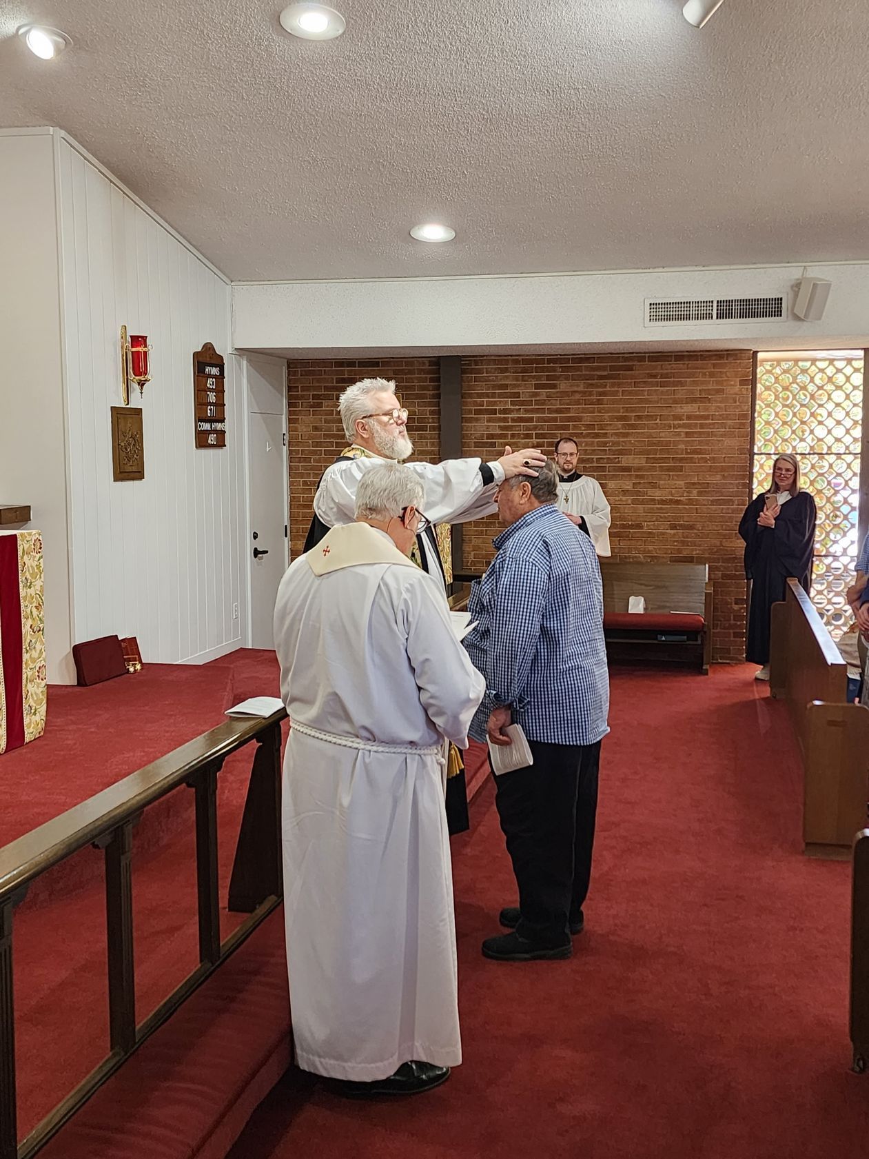 Clergy member anoints a person's head in a church during a religious ceremony. Others stand by.