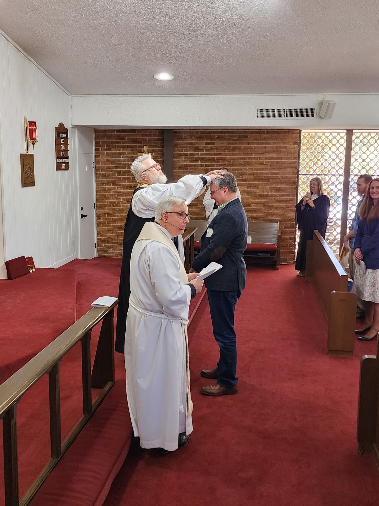 Priest anoints a man's head during a church ceremony. Others watch from the pews.