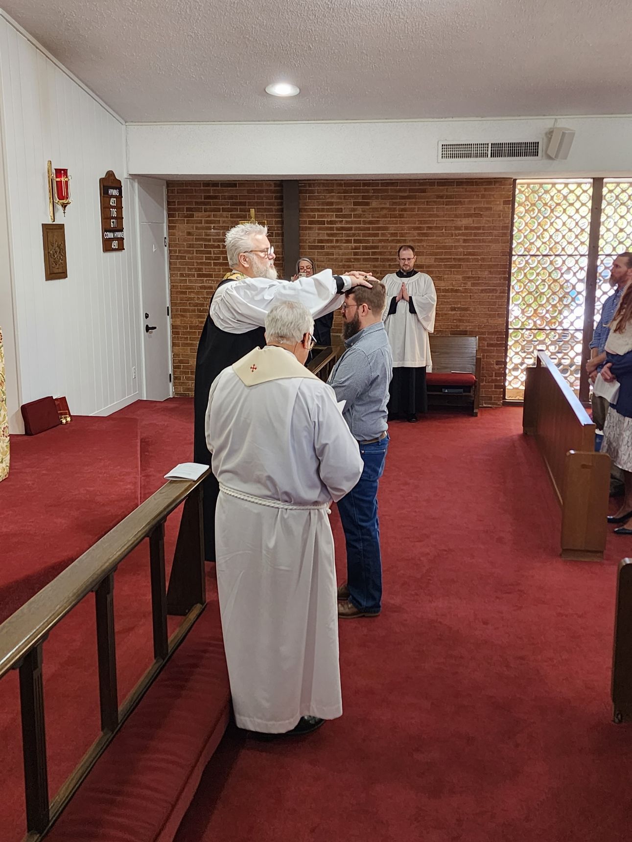 Clergyman anoints a man's head during a religious ceremony inside a church.