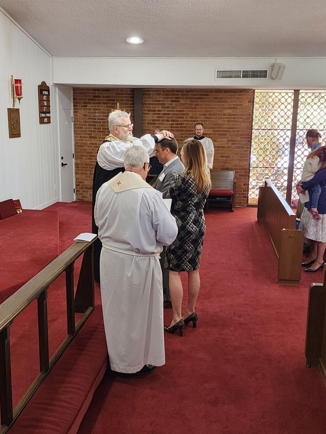 Clergy members lay hands on a man during a church ceremony; other attendees are present.